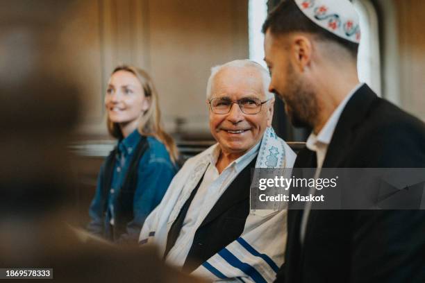 man talking with smiling senior male while sitting at synagogue - jewish prayer shawl stock pictures, royalty-free photos & images