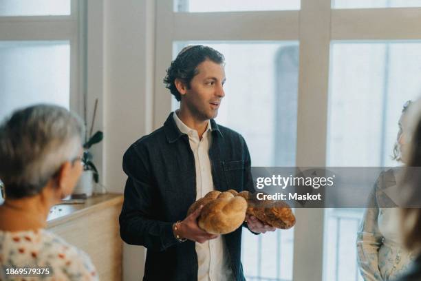 jewish man holding challah bread while talking with people during congregation at synagogue - kiddush cup stock-fotos und bilder
