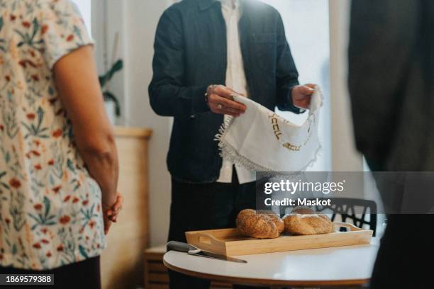 midsection of man holding challah cover over tray of bread during jewish congregation at synagogue - kiddush cup stock-fotos und bilder