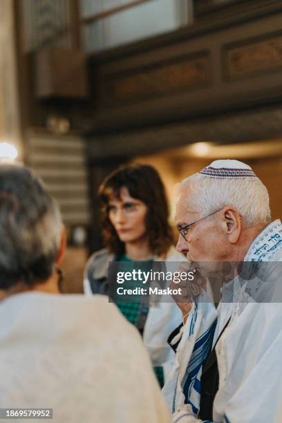 senior man wearing yarmulke while praying during jewish congregation at synagogue - jewish prayer shawl stock pictures, royalty-free photos & images