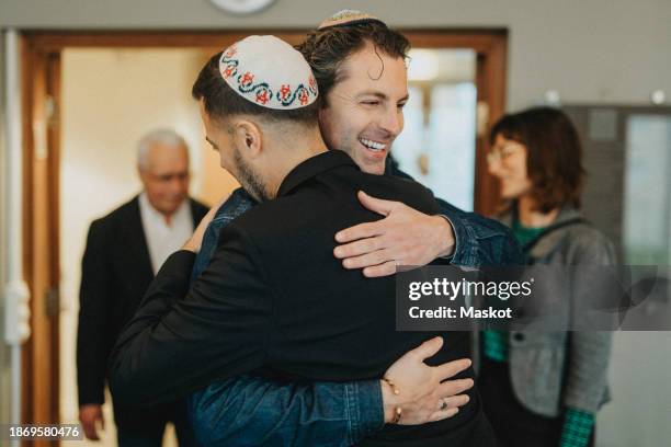 happy men wearing yarmulkes and greeting each other during jewish congregation at synagogue - judeus imagens e fotografias de stock