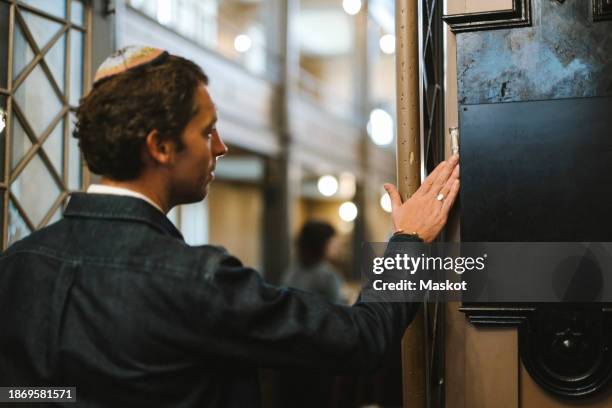 man wearing yarmulke and touching mezuzah while entering synagogue - jewish religion stock pictures, royalty-free photos & images