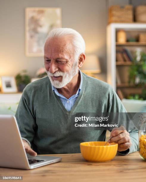retired man preparing cornflakes breakfast and using laptop to read new news - widower stock pictures, royalty-free photos & images