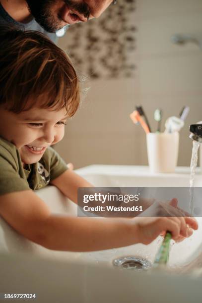 man with happy boy washing tooth brush in sink at home - running water bath stock pictures, royalty-free photos & images