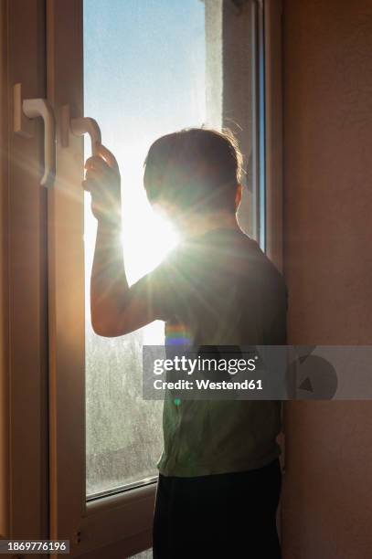 boy looking through window on sunny day - contraluz fotografías e imágenes de stock