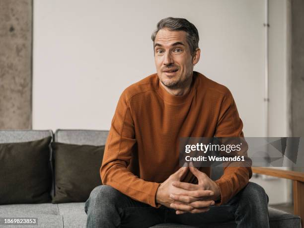 smiling man with hands clasped sitting at home - sleeve stock pictures, royalty-free photos & images