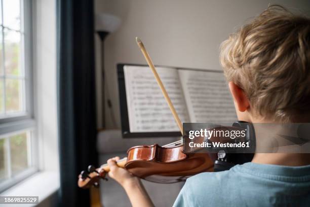boy practicing violin with sheet music at home - violino imagens e fotografias de stock