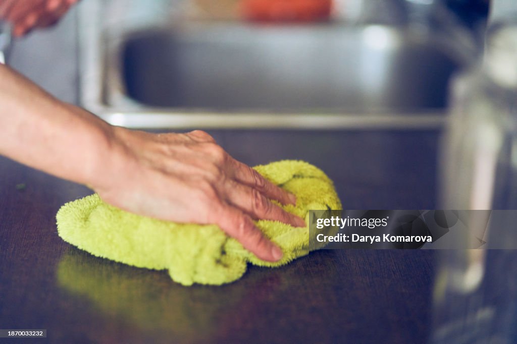 A woman wipes the table with a towel. A household routine for an elderly housewife.