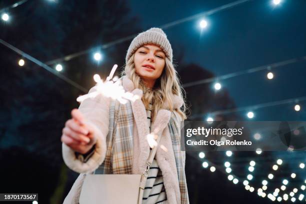 night christmas lights in the streets: woman celebrates the festival with a sparkler on the illuminated streets in winter - bengalischer feuer stock-fotos und bilder