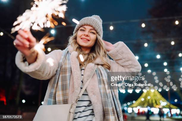 merry christmas walk with sparklers: woman with bengal fire strolls through the illuminated streets on christmas eve at night - bengalischer feuer stock-fotos und bilder