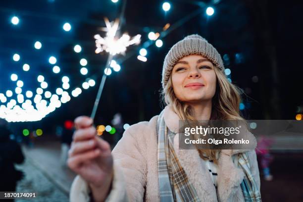 glowing christmas spirit with sparklers: woman wandering the nighttime streets alone under the street lights - bengalischer feuer stock-fotos und bilder