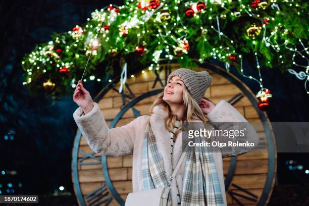 clock tower festivities on new year: smiling woman celebrates with sparklers in front of decorated clock on christmas eve - bengalischer feuer stock-fotos und bilder