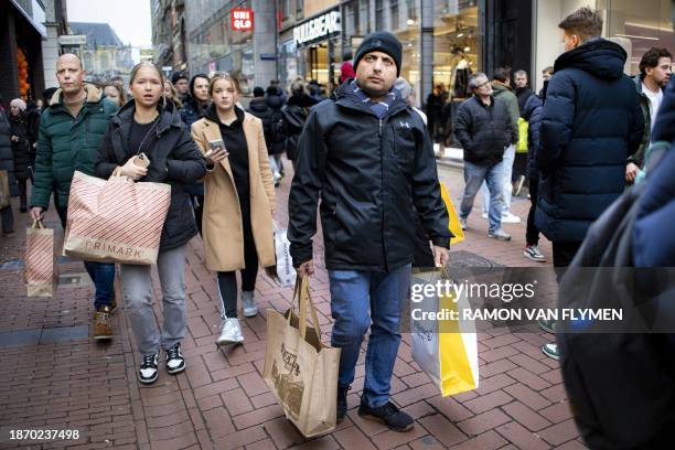 Shoppers hold bags as they walk in a street with shops, in the centre of Amsterdam on December 23, 2023. / Netherlands OUT