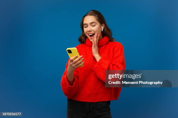 amazed emotional young woman looking smartphone in blue background - mono prenda de vestir fotografías e imágenes de stock