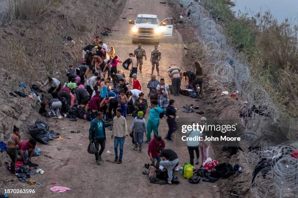 Seen from an aerial view, Texas National Guard troops look on as immigrants change into dry clothes after wading through the Rio Grande from Mexico...