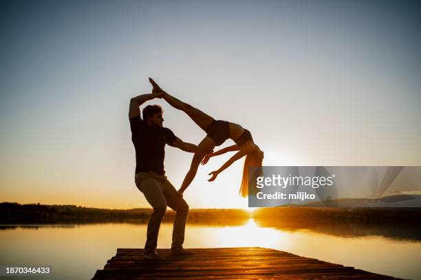 young man and woman doing acroyoga by lake - acroyoga stock pictures, royalty-free photos & images