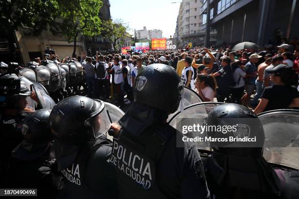 Protesters stand guard in front a line of police officers during a demonstration against President Javier Milei and recent announcements by Minister...