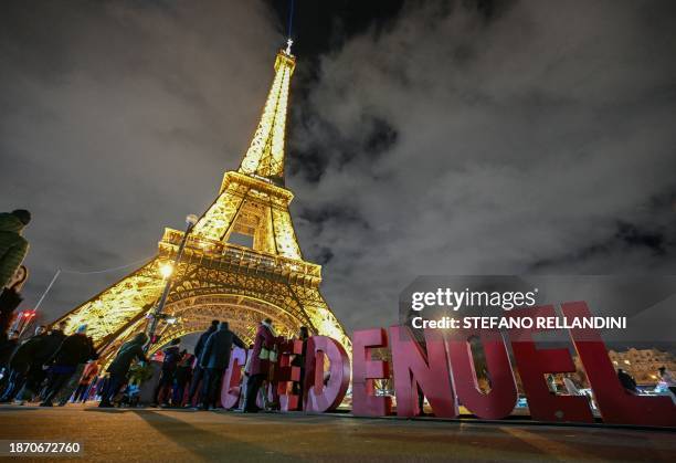 This photograph taken on December 23 shows a view of visitors walking past letters reading Noel with the Eiffel Tower monument in the background, in...