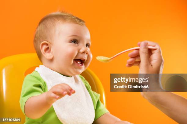 feeding cheerful baby on orange background - pureed stock pictures, royalty-free photos & images