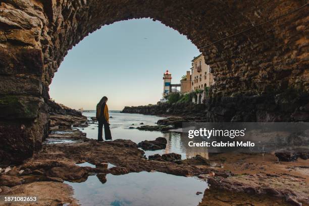 woman under the bridge with views of santa marta lighthouse in cascais - cascais stockfoto's en -beelden