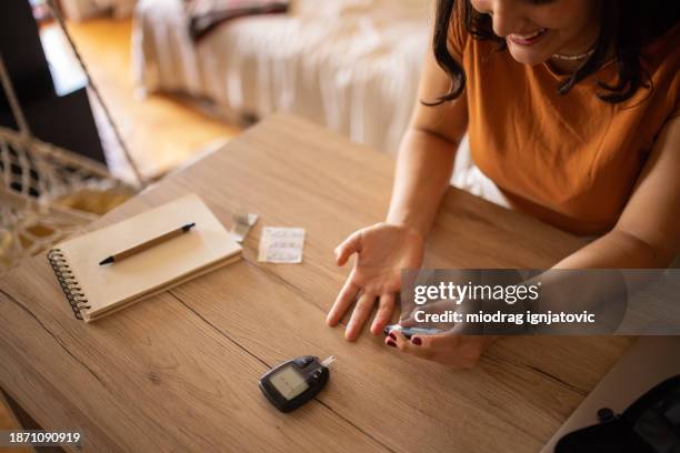 mujer joven comprobando el nivel de azúcar en sangre - glycemia fotografías e imágenes de stock