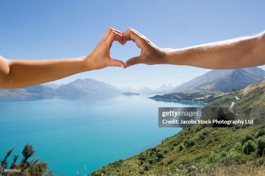 Caucasian couple making heart with hands in rural landscape