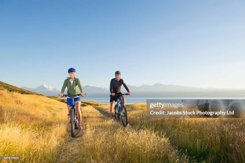 Caucasian couple riding bicycles in rural field