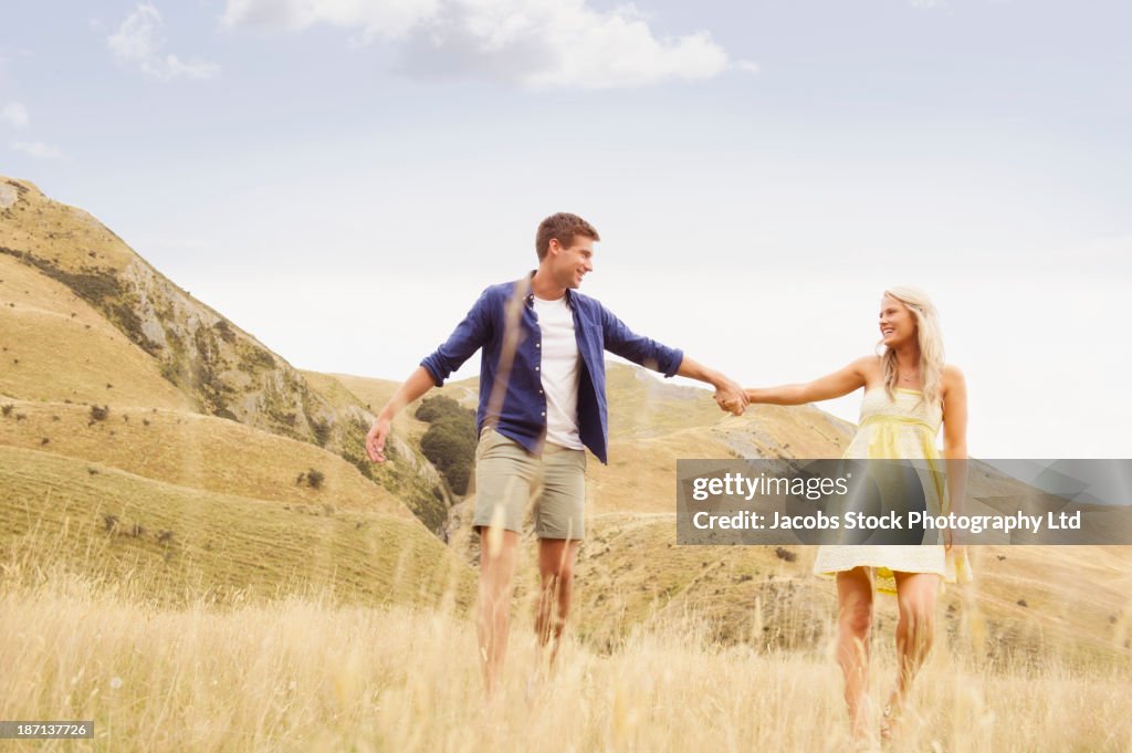 Caucasian couple holding hands in rural landscape