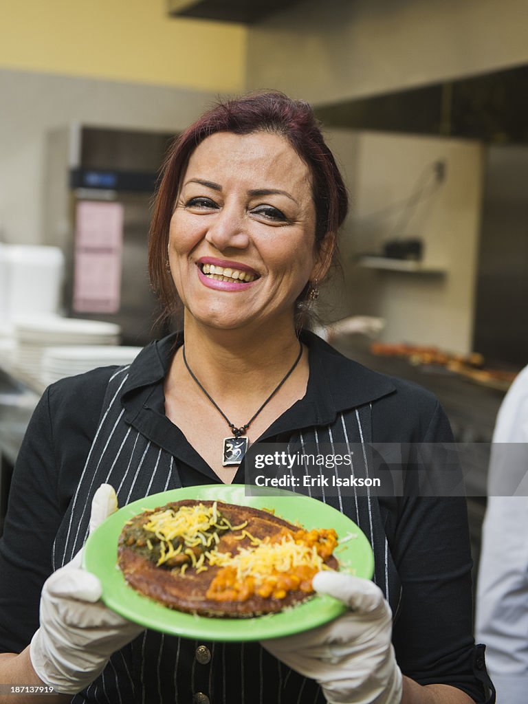 Mixed race chef holding plate of food in kitchen