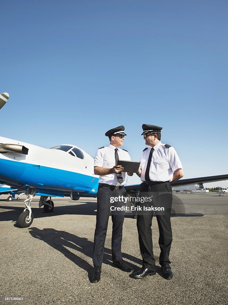 Caucasian pilots using digital tablet on runway