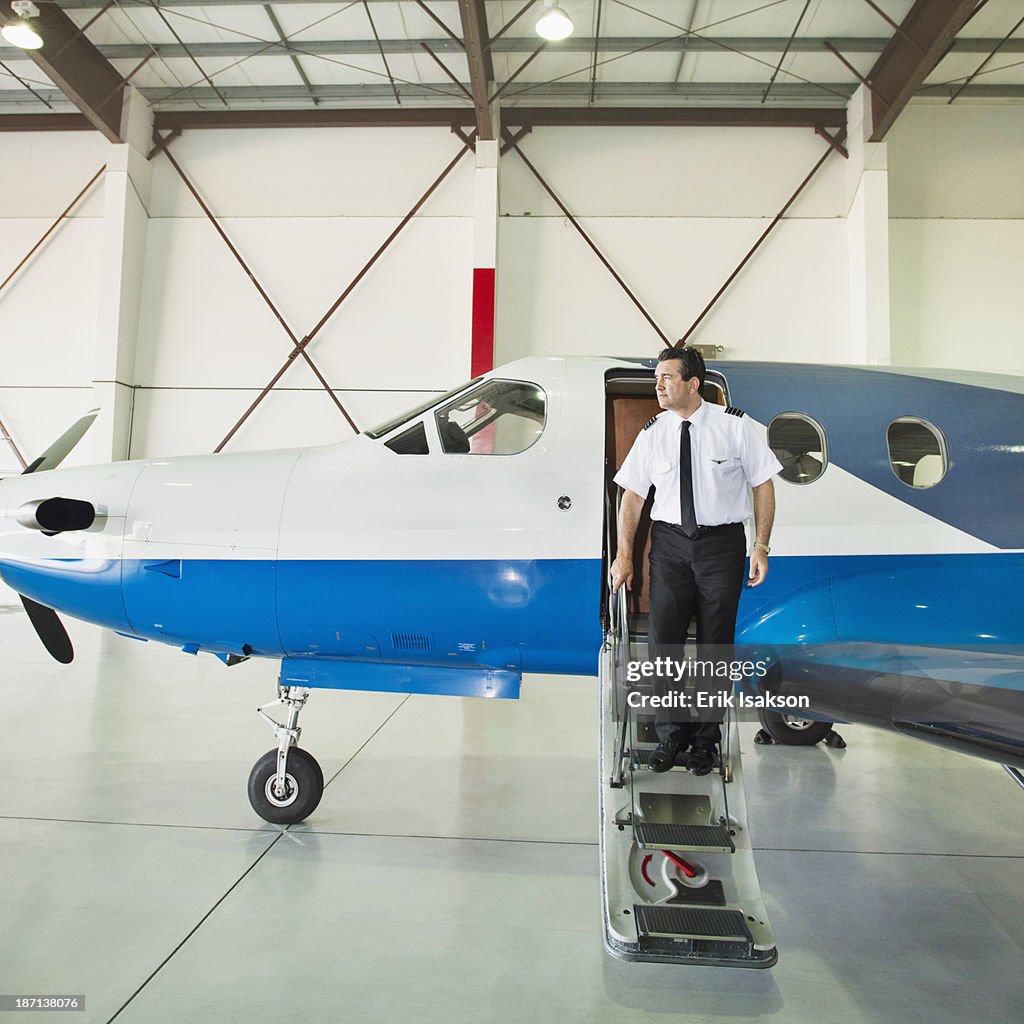 Caucasian pilot disembarking airplane in hangar