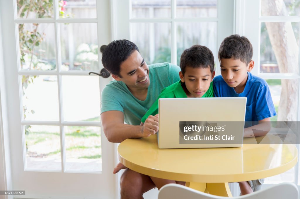 Hispanic father and sons using laptop