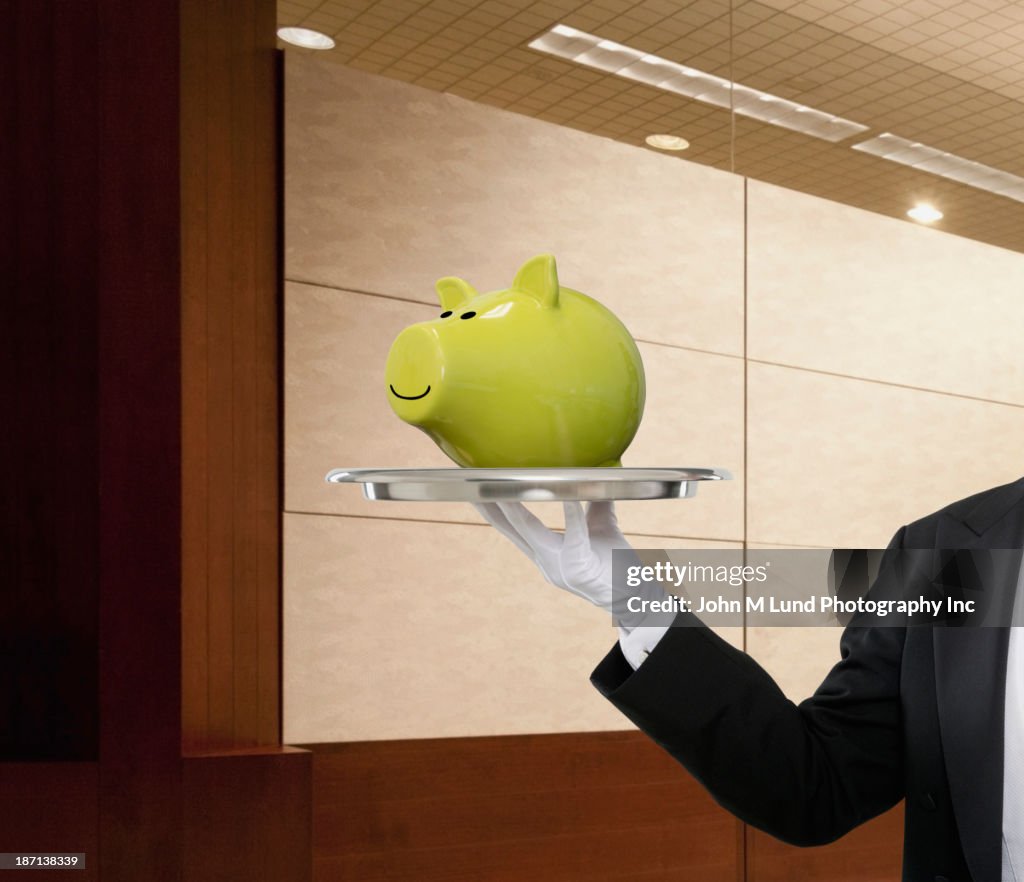 Waiter holding piggy bank on serving tray