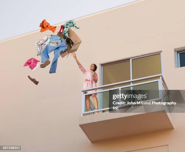 mixed race woman throwing clothes off balcony - clothes waste stock-fotos und bilder