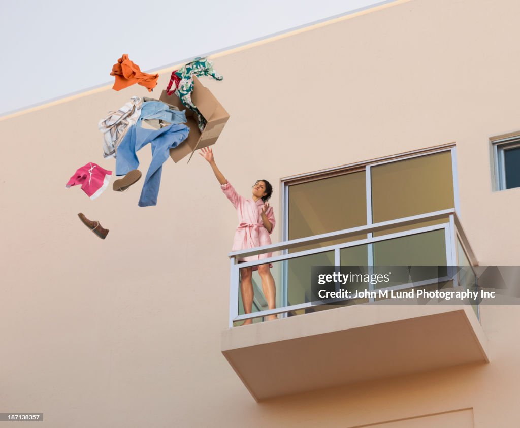 Mixed race woman throwing clothes off balcony