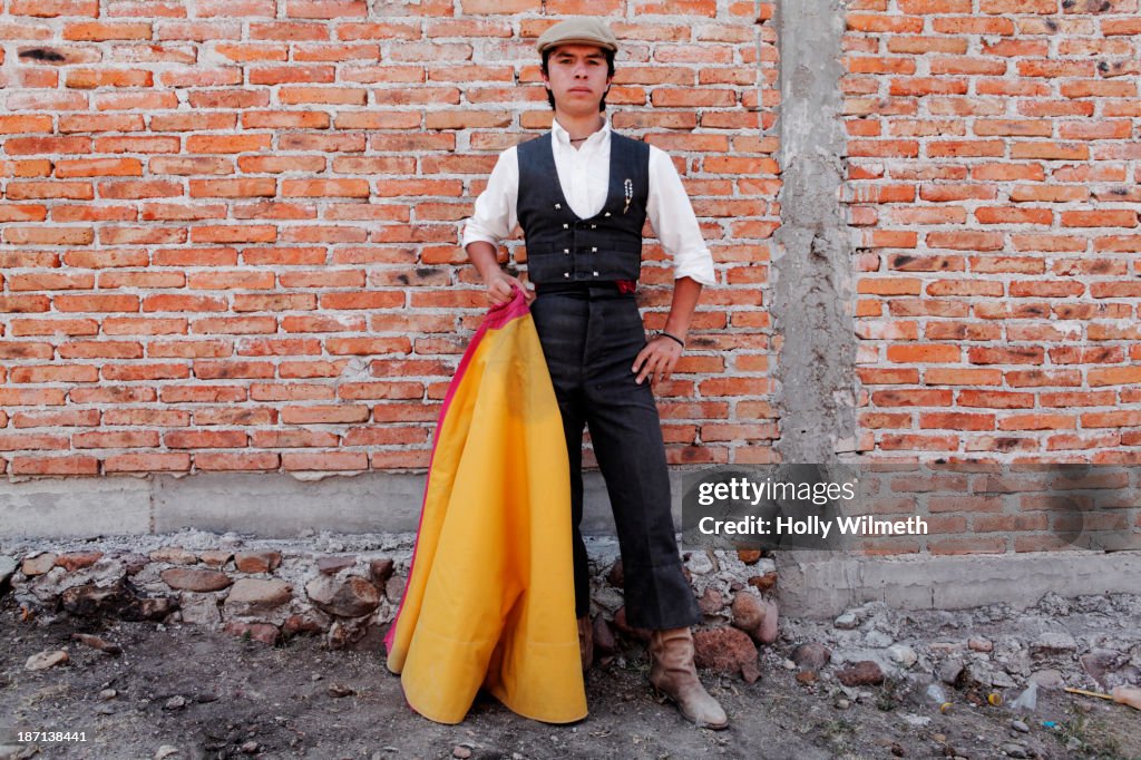 Man holding bullfighting cape in front of brick wall