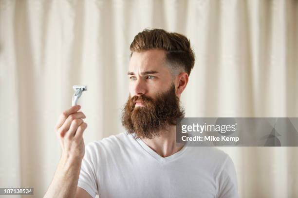 bearded caucasian man examining razor - barbear imagens e fotografias de stock