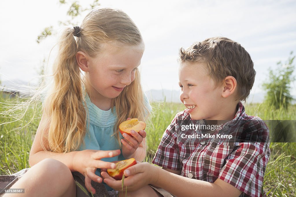 Caucasian children sharing fruit outdoors