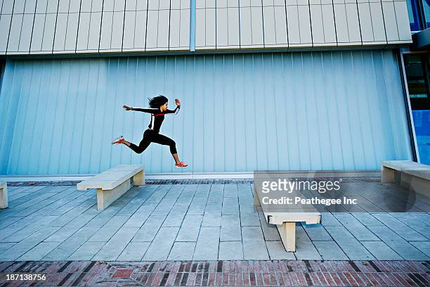 mixed race woman running on city street - hurdling track event stock-fotos und bilder