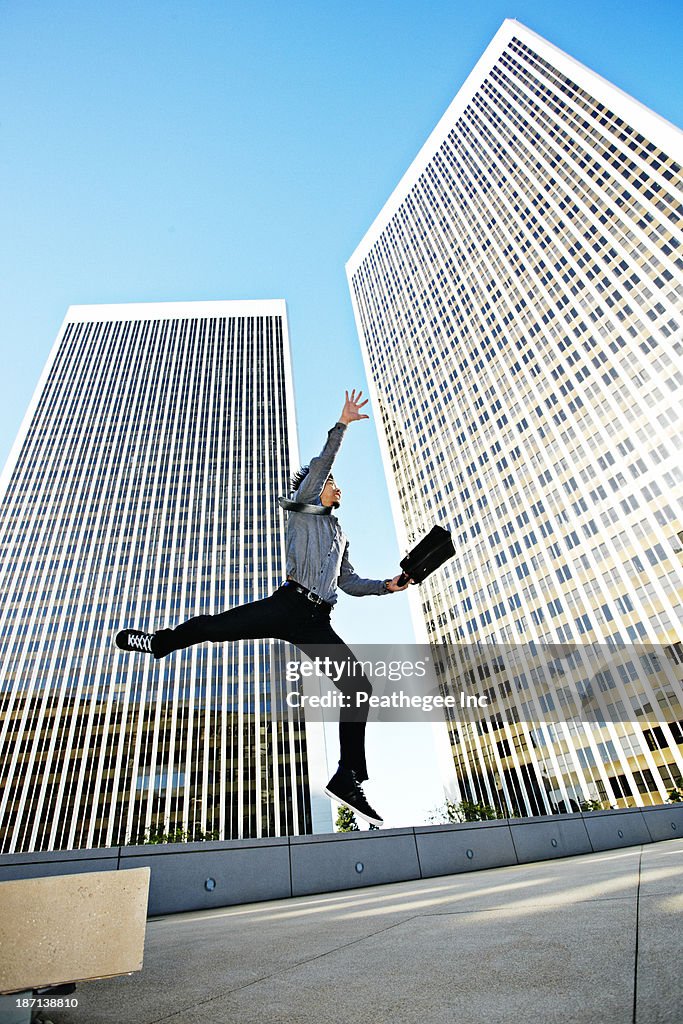 Asian businessman leaping on urban rooftop