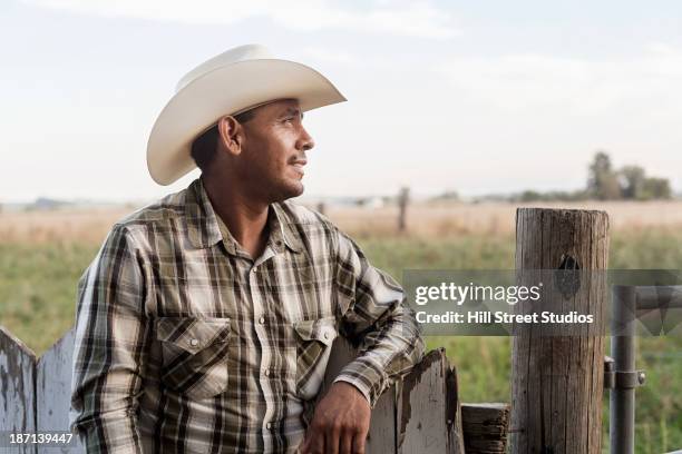 hispanic man leaning on wooden fence - cowboy hat foto e immagini stock