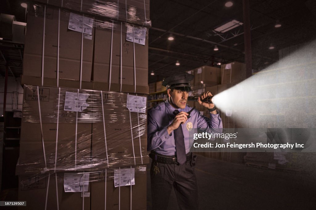 Police officer shining flashlight in warehouse