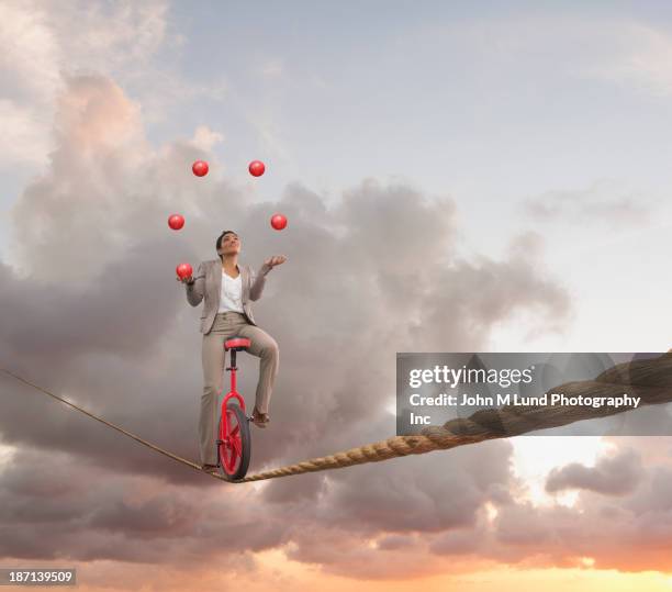 mixed race businesswoman juggling on tightrope on unicycle - jonglieren stock-fotos und bilder