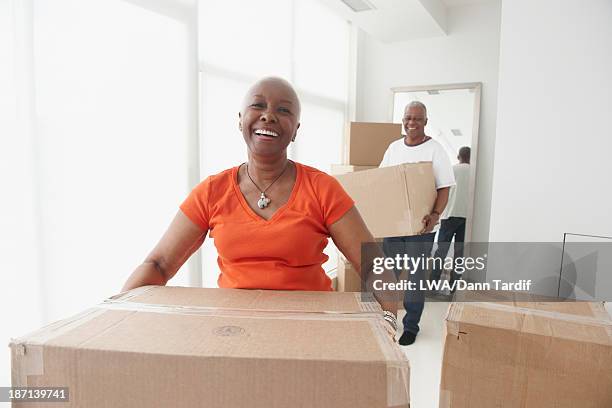 black couple carrying boxes in new home - senior moving house stock pictures, royalty-free photos & images