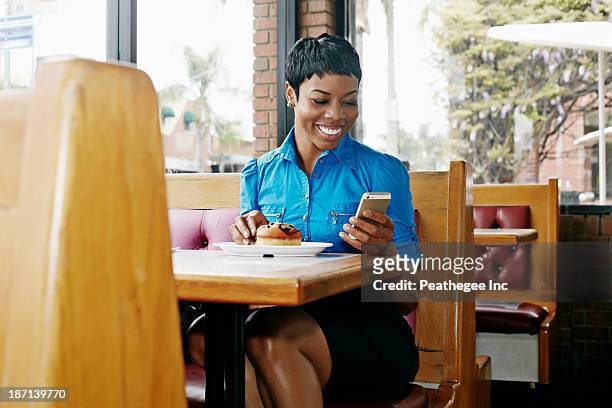 african american businesswoman using cell phone in restaurant - african american restaurant texting stockfoto's en -beelden