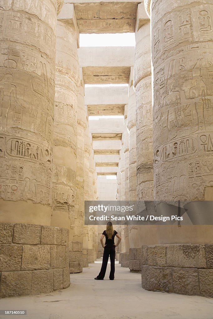 A Woman Tourist Stands At The Base Of The Massive Columns In The Temples Of Karnak On The East Bank Of Luxor Along The Nile River
