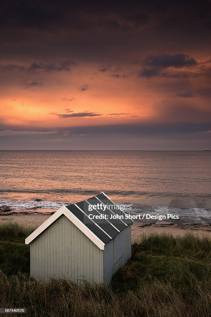 A Small Building Along The Water With A Pink Sky At Sunset