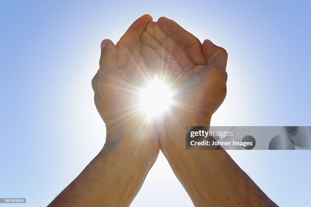 Person cupping hands against sky as to hold sun in between