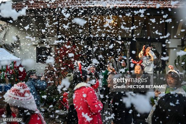People are seen in the garden of a flower shop where a sprayer shoots foam that simulates snow in the Jing' an district in Shanghai on December 24,...