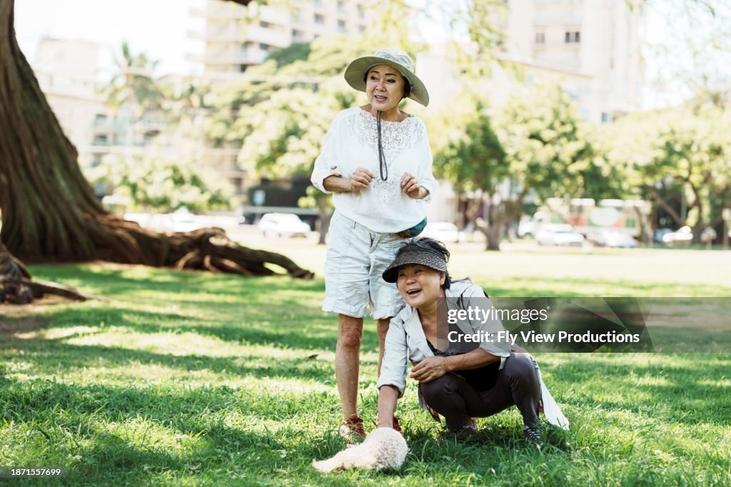 Korean woman petting her dog while at the park with a friend